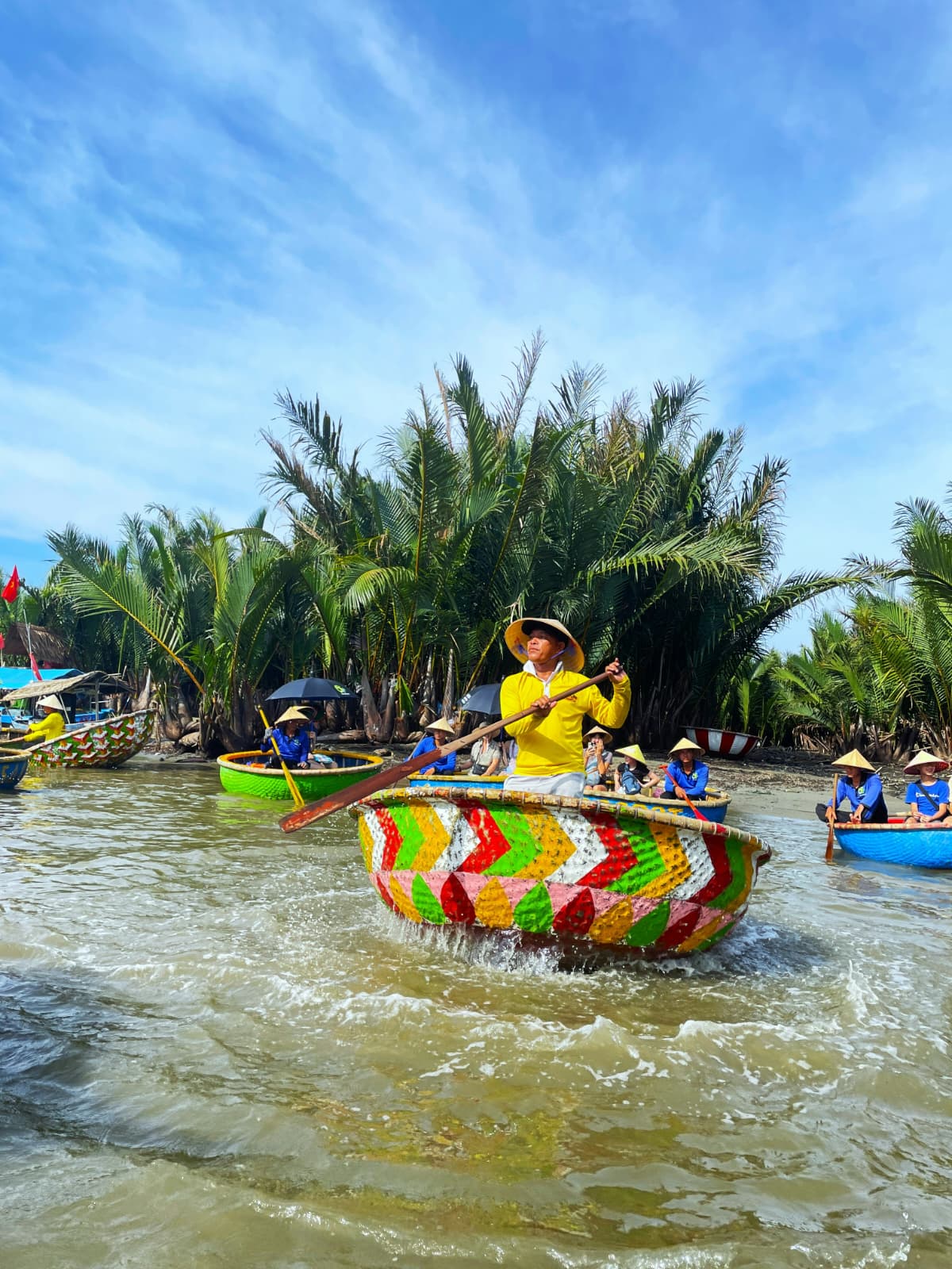 Boatman in yellow spinning a colorful basket boat, with more basket boats and coconut palms behind