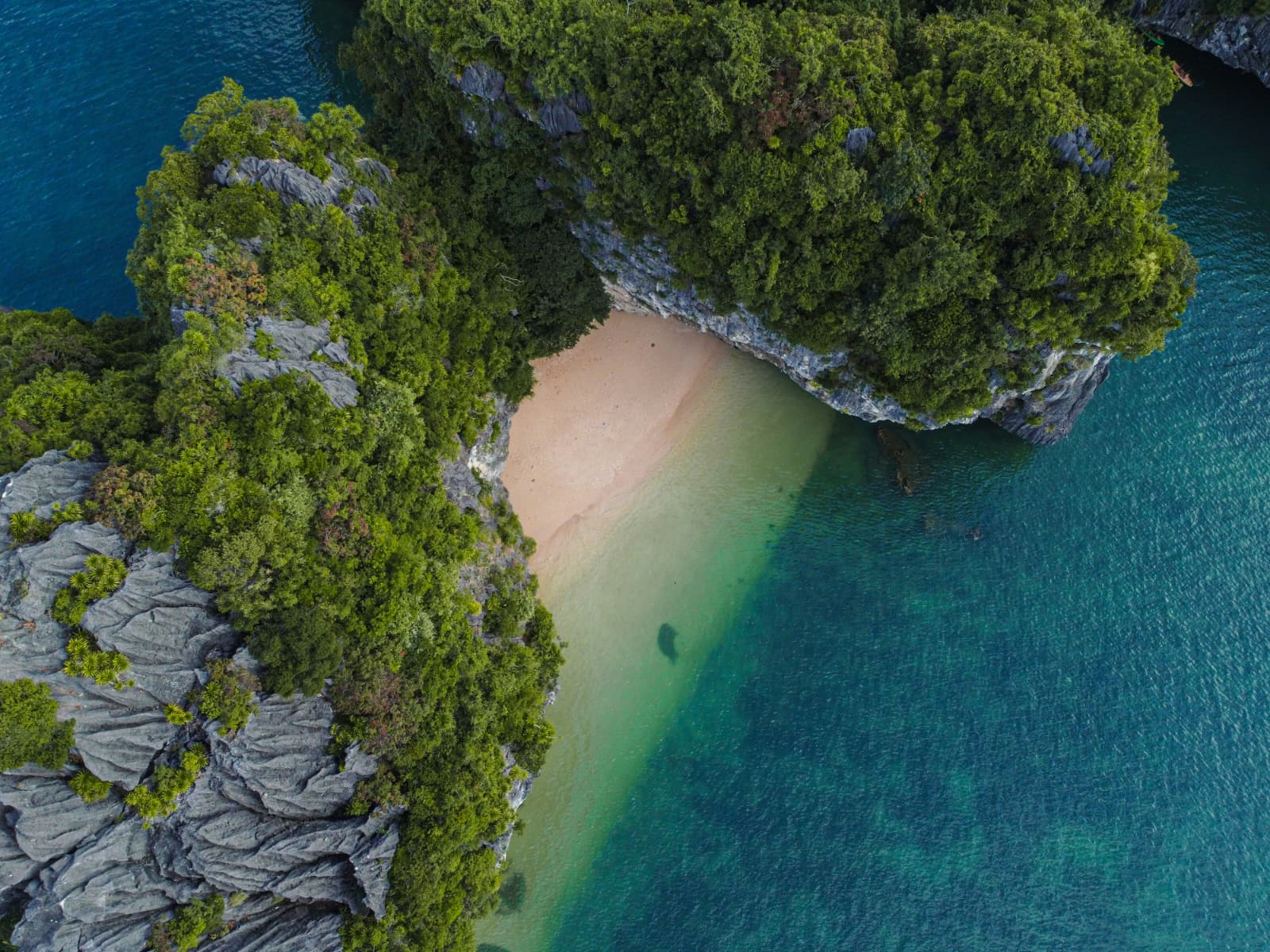 Aerial view of a hidden sandy beach between forested limestone islands near Cat Ba