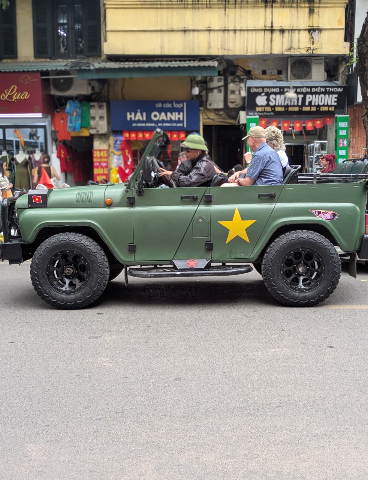 Tourists riding in an open-top green army Jeep through Hanoi's Old Quarter